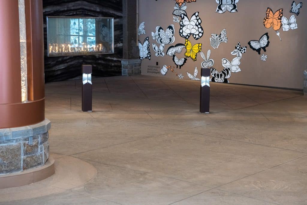 Detailed view of textured sandscape concrete and a square ground light, with a butterfly mural in the background.