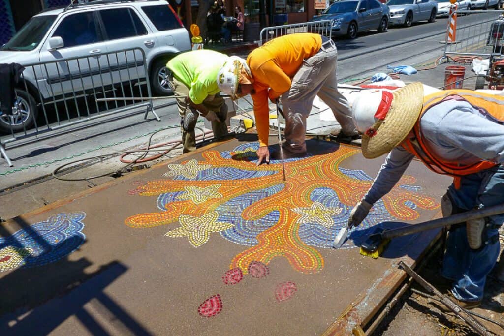 A group of three individuals working on a colorful Litho mosaic installation.